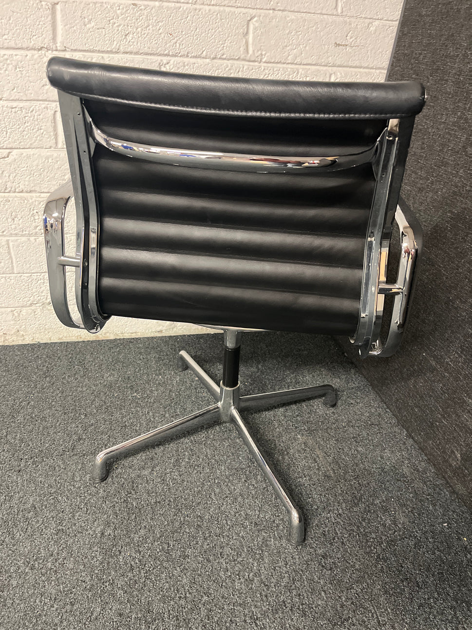 Eames style black leather low back swivel chair with polished chrome base on pads or castors