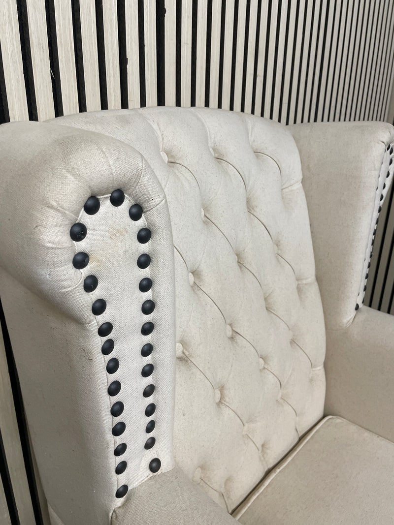Beige tufted wingback armchair with decorative black nailhead trim detail.  44518